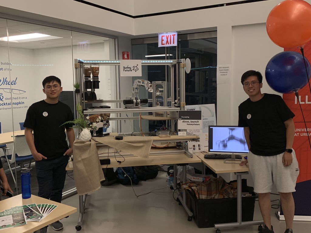 Both founders flanking the prototype at a UIUC demo night, Alexa placard on the rig