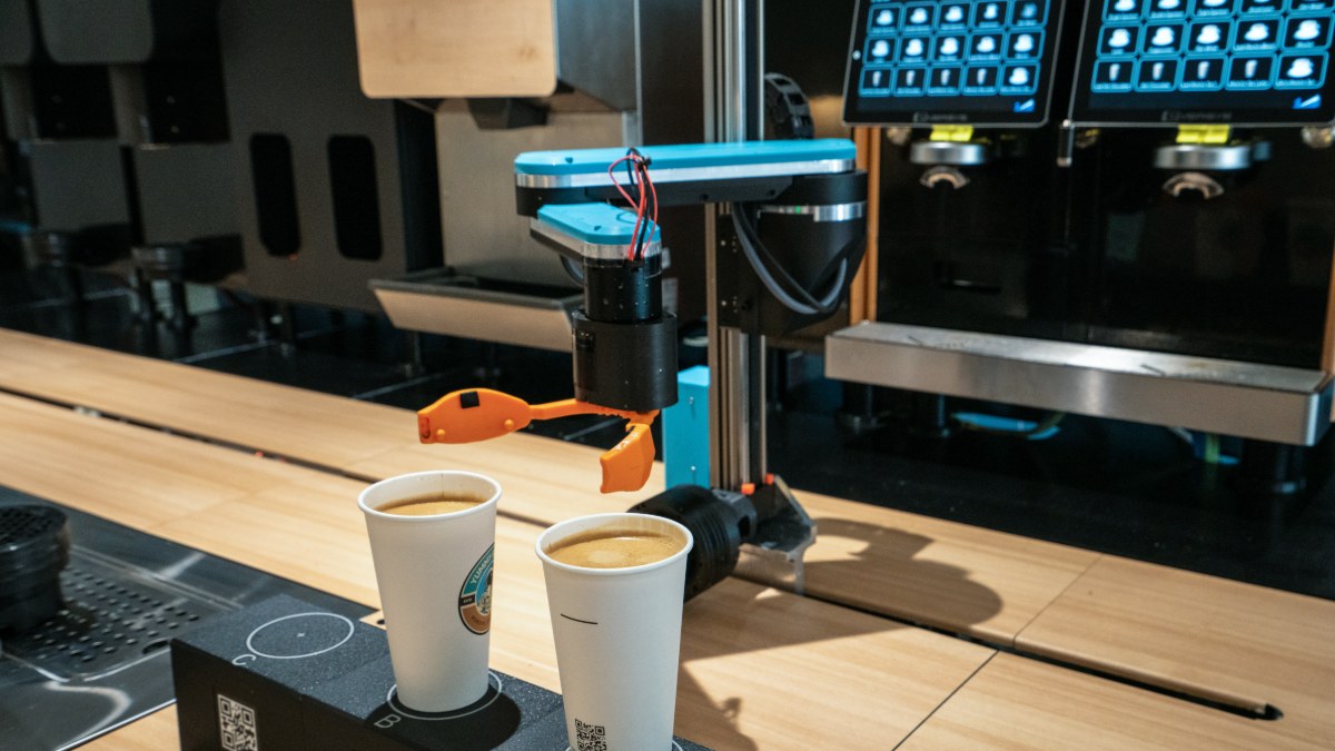 Robot arm with orange gripper over two finished coffees at the production bar