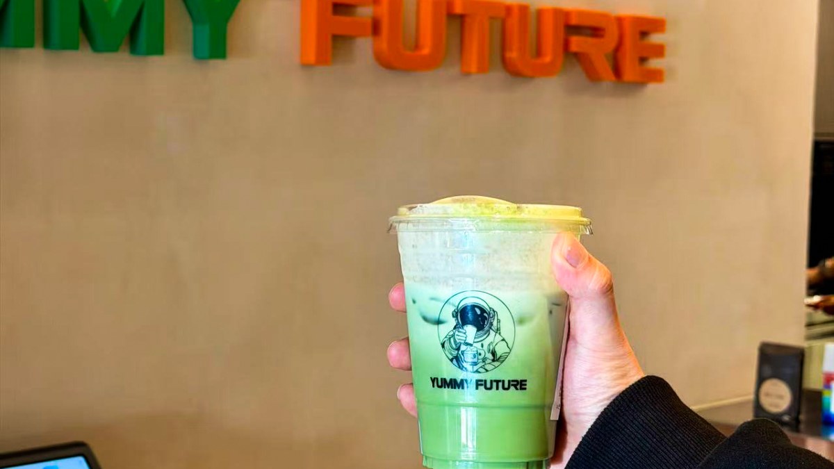 Customer holds a Yummy Future iced matcha cup directly under the orange FUTURE wordmark on the wall