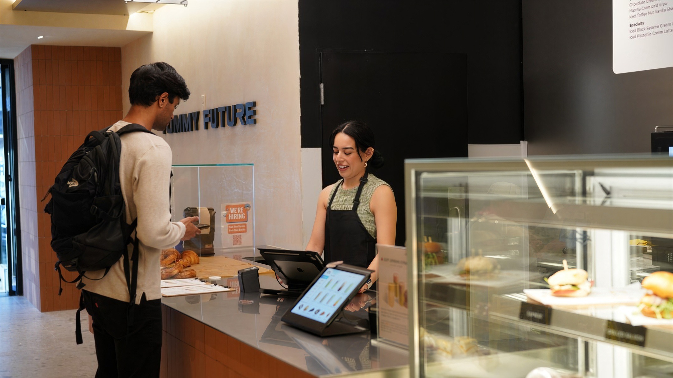 A customer ordering at the counter while a staff member takes the order on a tablet, under the Yummy Future wall sign