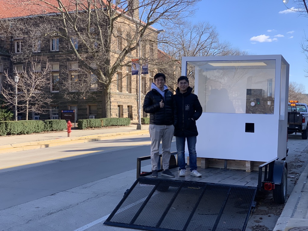 The two founders on the trailer bed with the white robotic coffee kiosk, UIUC campus